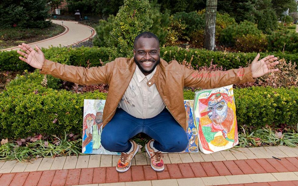 young man smiling with two of his paintings