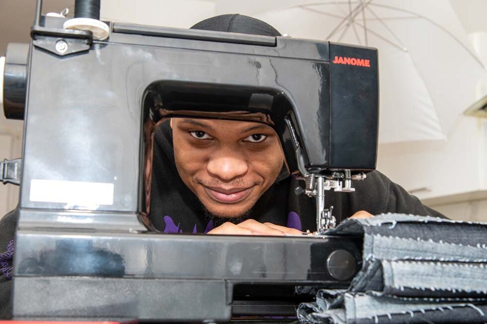 young man smiling from behind a sewing machine